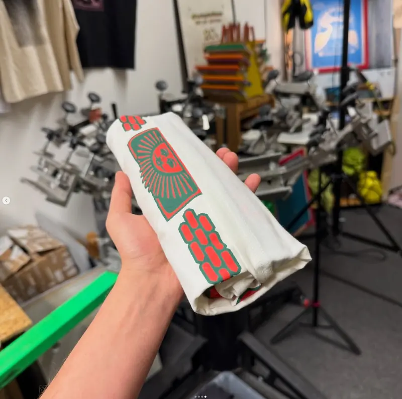 Hand hält ein frisch bedrucktes Shirt vor der Werkstattwand